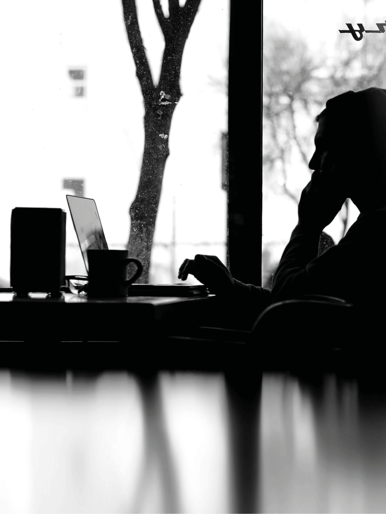 Silhouette einer Person am Laptop vor einem Fenster
