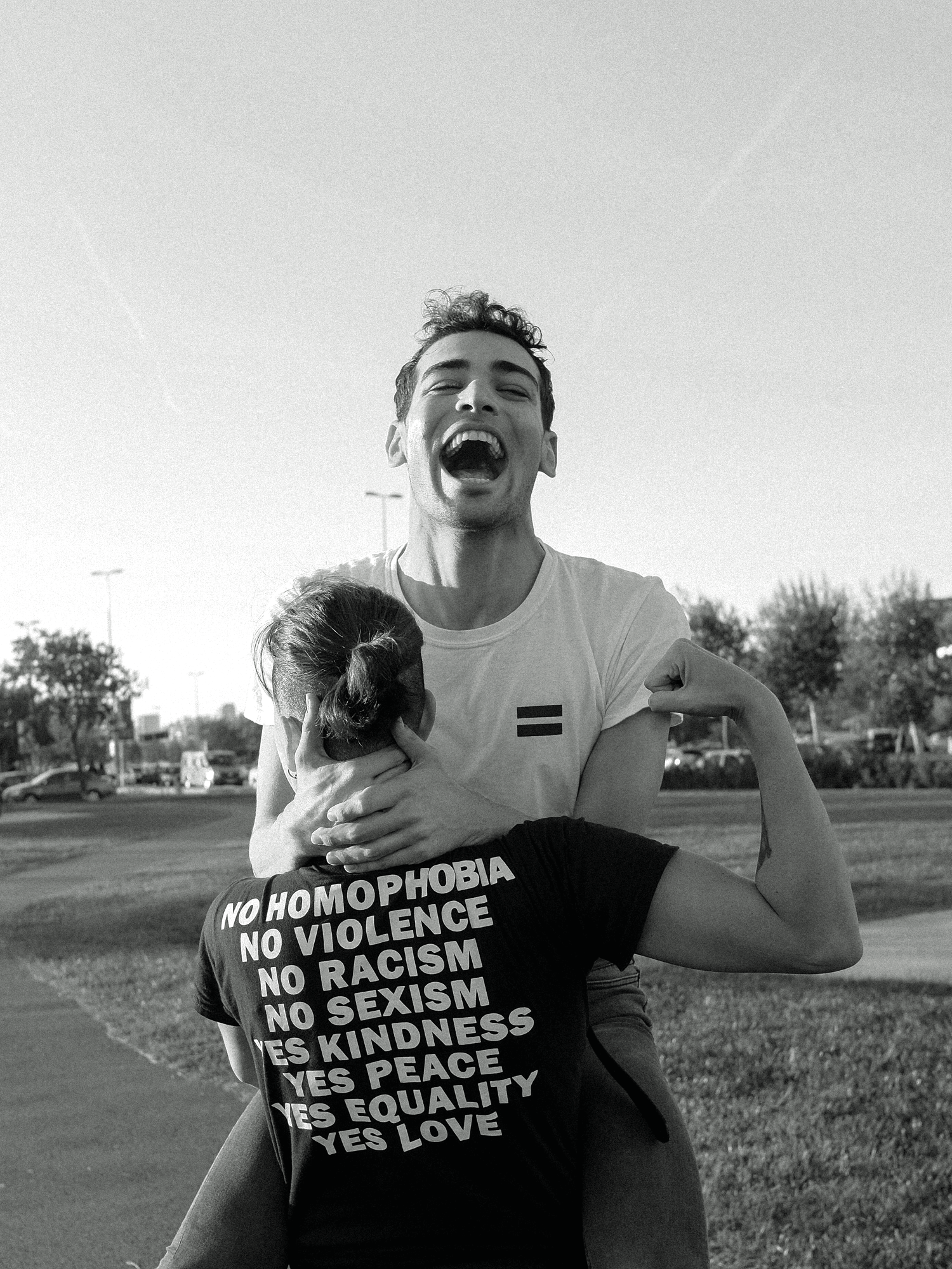 Lachender Mann trägt ein Kind, Shirt mit Aufschrift gegen Homophobie, Gewalt und Rassismus