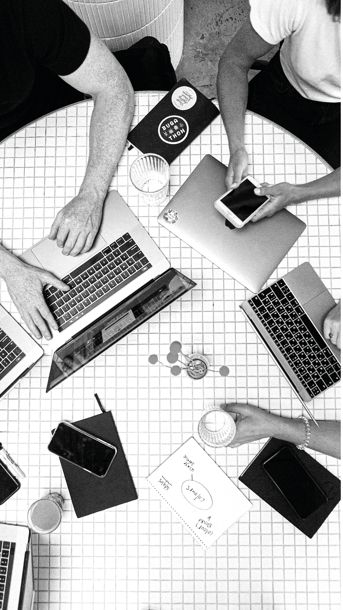 Hände an Laptops und Smartphone auf einem gefliesten Tisch, von oben